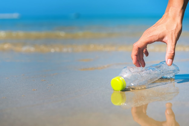 Cerca del hombre de la mano recogiendo limpieza de botellas de plástico en la playa