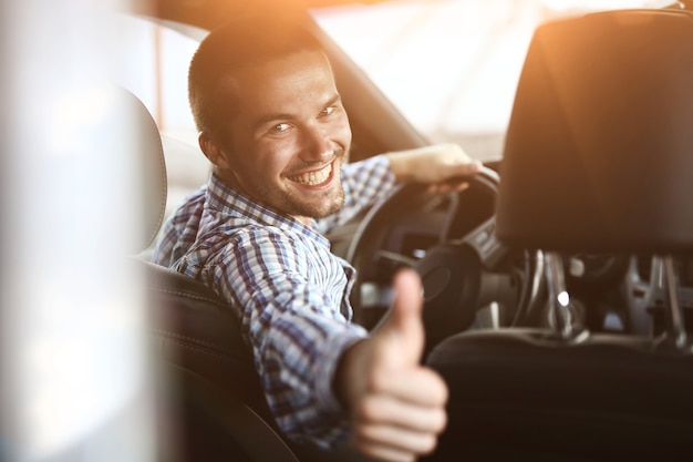 Foto de cerca. hombre moderno sentado en un coche y mostrando su pulgar hacia arriba.