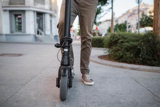 Cerca del hombre montando patinete eléctrico negro en el paisaje urbano al atardecer