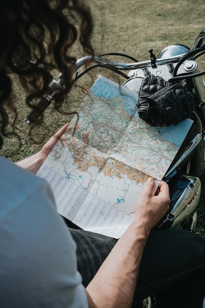 Cerca de un hombre en una motocicleta comprobando un mapa mientras realiza un viaje por carretera. Concepto de viaje. Guantes y manos groseras sosteniendo un mapa sobre una moto de la vieja escuela.