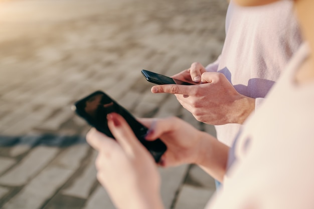 Cerca del hombre y la mujer usando teléfonos inteligentes mientras está de pie al lado del otro al aire libre