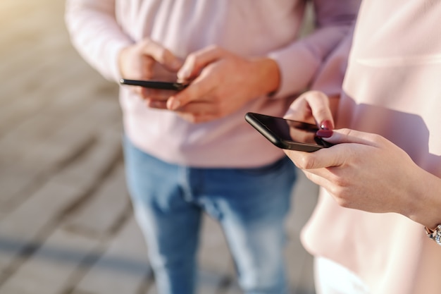 Cerca del hombre y la mujer usando teléfonos inteligentes mientras está de pie al lado del otro al aire libre
