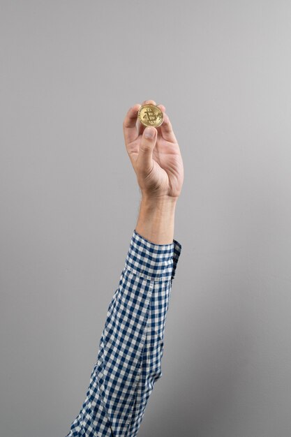 Foto cerca del hombre que sostiene la moneda de oro de bitcoin sobre fondo gris. dinero digital dentro de la red blockchain.
