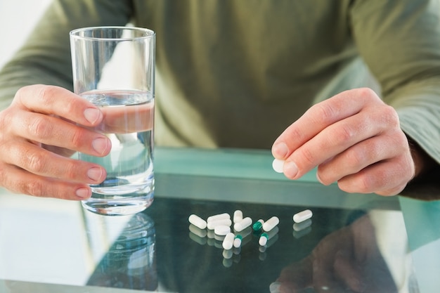 Cerca del hombre que sostiene una pastilla y un vaso de agua