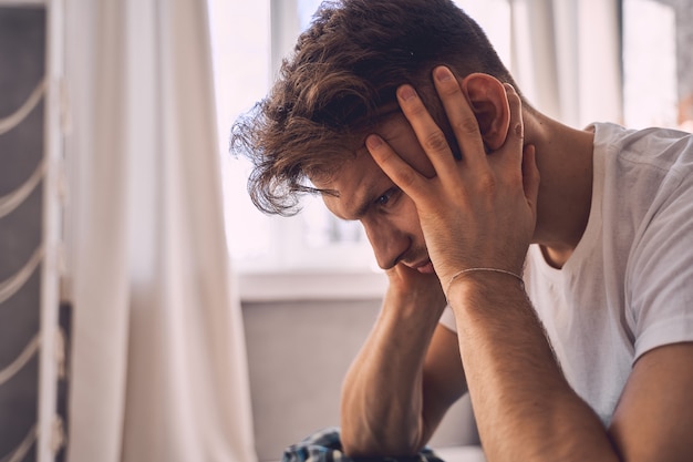 Cerca de hombre serio que sentado en posición semi y profundo en pensamientos