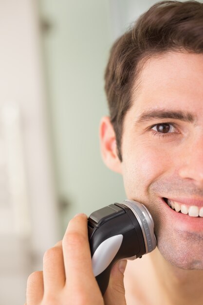 Cerca del hombre sonriente que afeita con la maquinilla de afeitar eléctrica