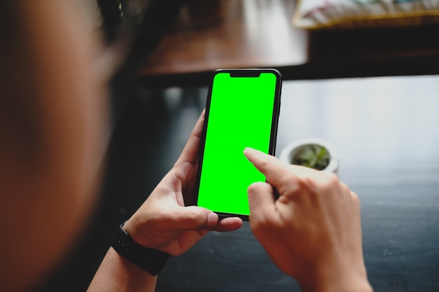 Foto cerca del hombre usando productos de orden de teléfono celular de pantalla verde en blanco para comprar en línea dentro de la cafetería.