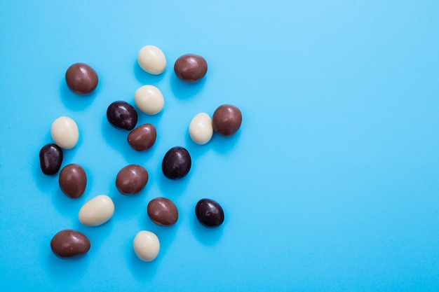 Cerca de huevo de chocolate y dulces gotas sobre superficie azul