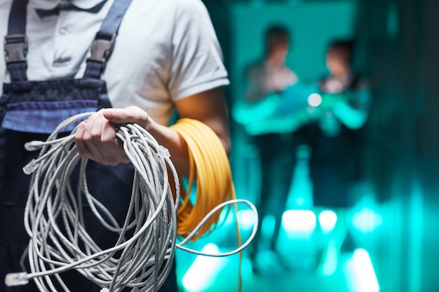 Cerca del ingeniero de redes sosteniendo cables en la sala de servidores durante los trabajos de mantenimiento en el centro de datos, espacio de copia