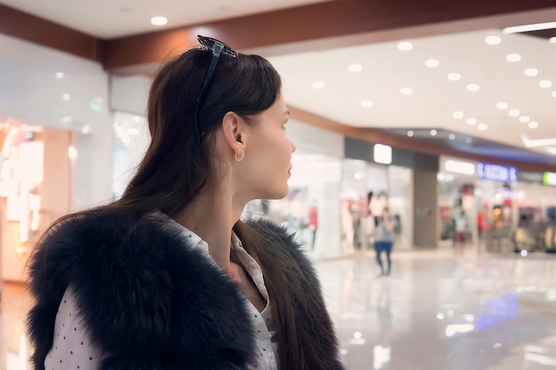 Cerca de joven brunet en centro comercial mirando a la cámara. Mujer guapa se encuentra en la zona a pie del centro comercial y mira a lo lejos. Chica busca algo en el centro comercial.