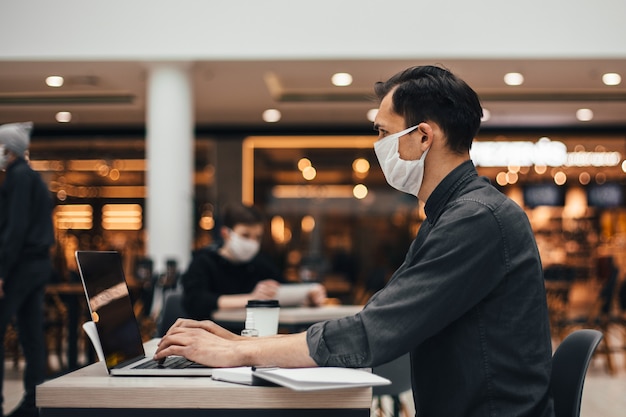 De cerca. un joven con una computadora portátil está trabajando sentado en una mesa en un café