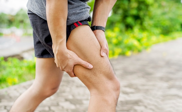 Cerca del joven deportista asiático tiene dolor en los músculos y las articulaciones durante el ejercicio al aire libre, durante el entrenamiento o correr y el concepto de deporte injuty