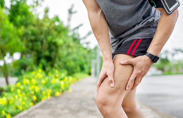 Cerca del joven deportista asiático tiene dolor en los músculos y las articulaciones durante el ejercicio al aire libre, durante el entrenamiento o correr y el concepto de deporte injuty