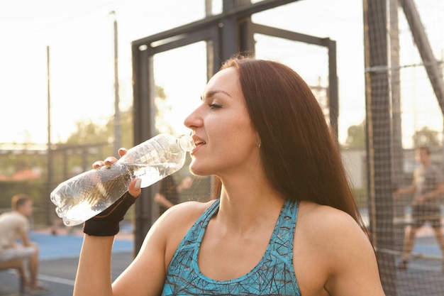 Cerca de una joven deportista bebiendo agua en el patio de recreo de la calle al atardecer