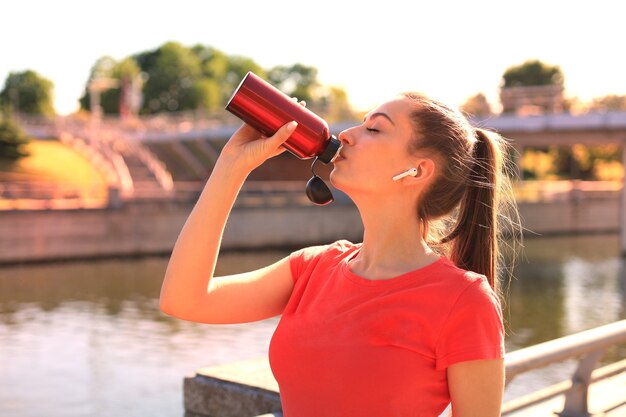 Cerca de una joven deportista cansada atractiva al aire libre, bebiendo agua de una botella.