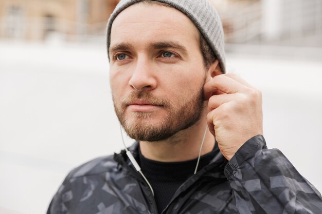 Cerca de un joven deportista motivado escuchando música con auriculares mientras está de pie en el estadio