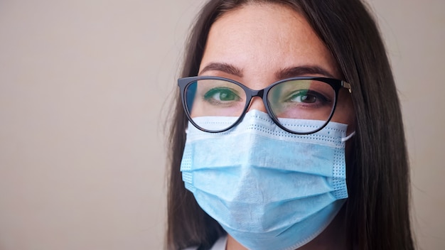 Cerca de la joven doctora morena con gafas y máscara protectora azul claro copyspace