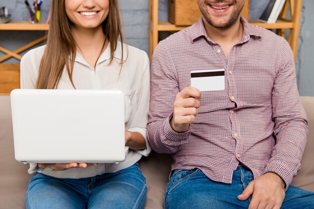 Cerca de la joven familia feliz con portátil y tarjeta bancaria