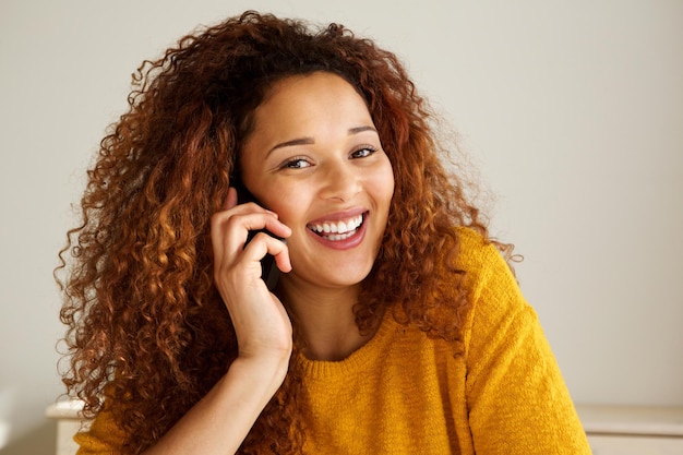 Cerca de una joven feliz de raza mixta sonriendo y hablando por teléfono móvil