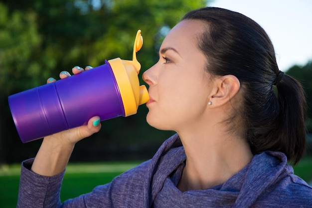 Cerca de una joven hermosa mujer bebiendo agua de una botella en el parque