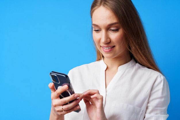 Cerca de la joven mujer rubia con su smartphone contra el fondo azul.