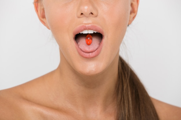 Cerca de una joven mujer en topless aislada, sosteniendo la cápsula de la píldora en su lengua