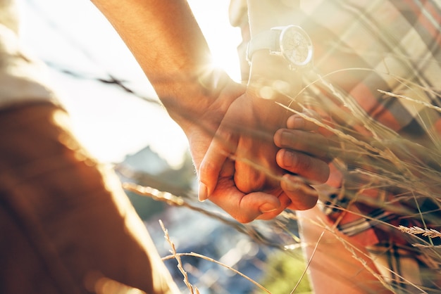 Cerca de la joven pareja amorosa en ropa casual tomados de la mano mientras está de pie al aire libre