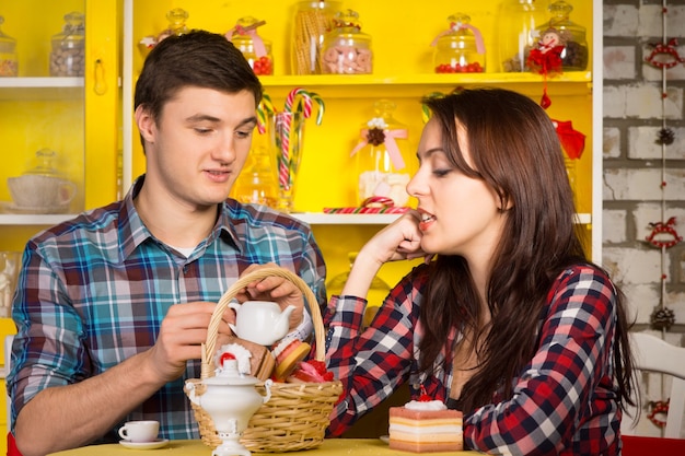 Cerca de joven pareja blanca en camisas a cuadros que datan en el café con canasta de pastelería y bebidas calientes. Capturado con tarros de caramelo en la parte posterior.