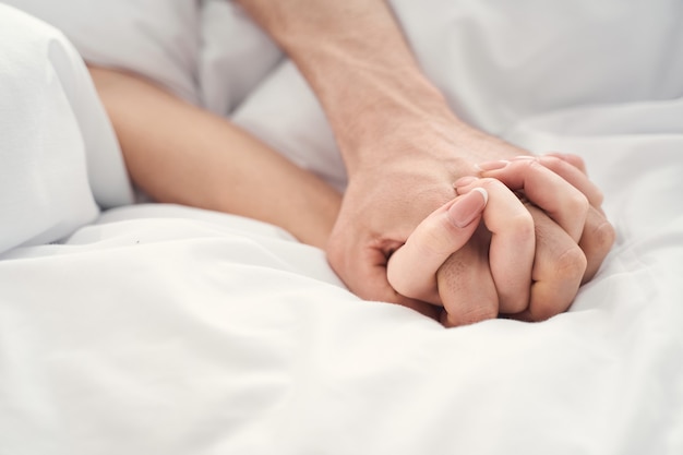 Cerca de una joven pareja casada cogidos de la mano durante el momento de la intimidad en la cama