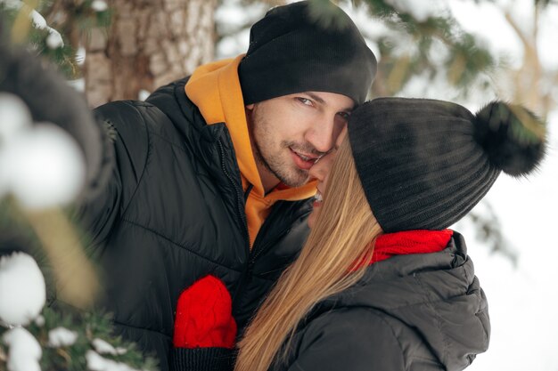 Cerca de la joven pareja en ropa de abrigo de pie juntos en un parque de invierno