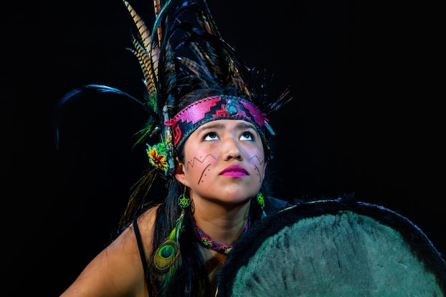 Foto cerca de la joven teotihuacana, xicalanca - tolteca en fondo negro, con vestimenta tradicional danza con adornos con plumas y tambor