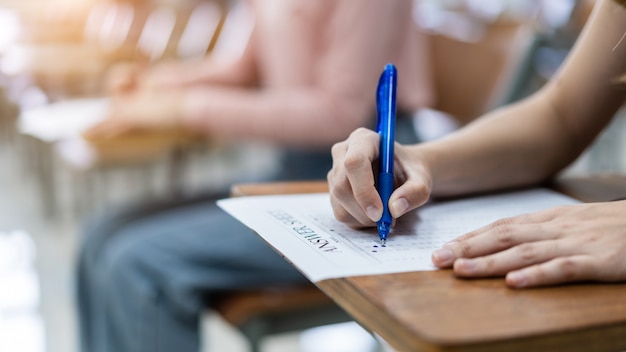 Cerca de jóvenes estudiantes universitarias se concentran en hacer exámenes en el aula. La alumna escribe la respuesta de los exámenes en la hoja de respuestas en el aula.