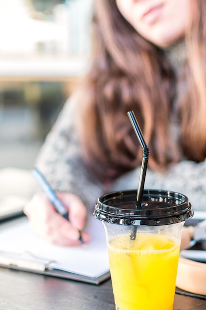 Cerca de jugo de naranja fresco en un vaso de plástico con tapa y paja en el escritorio de los estudiantes