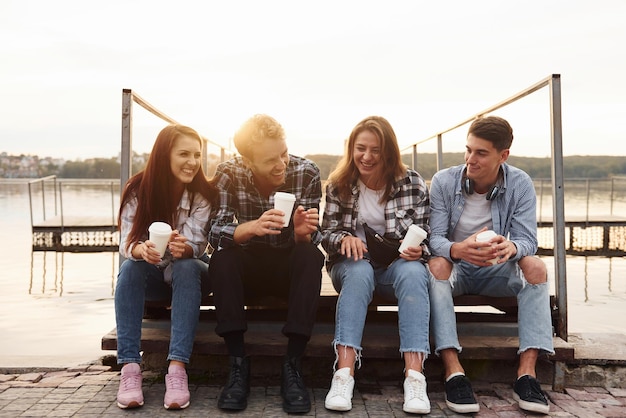 Foto cerca del lago grupo de jóvenes amigos alegres que están al aire libre divirtiéndose juntos