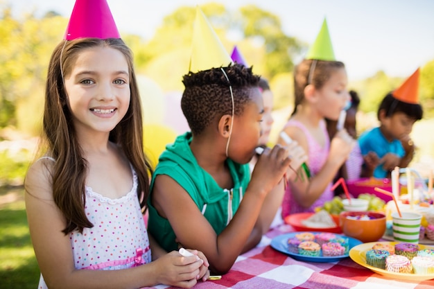 Foto cerca de linda chica sonriendo frente a otros niños durante una fiesta de cumpleaños