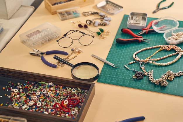 Foto cerca del lugar de trabajo de fabricación de joyas enhebrando un cordón en alambre con pinzas de joyería