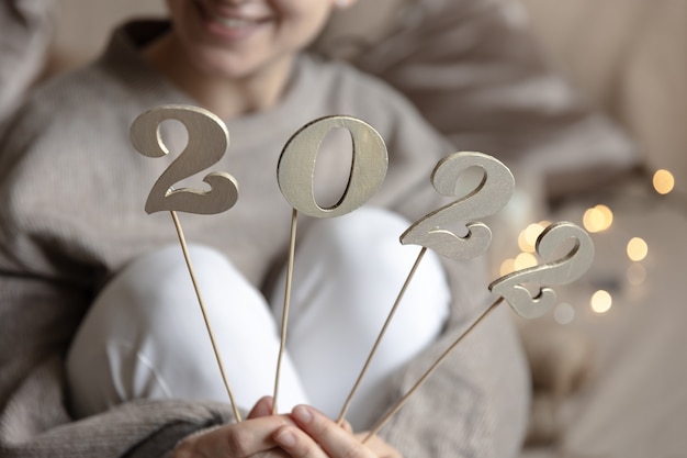 Cerca de madera números 2022 en palos en manos femeninas sobre fondo borroso con bokeh.