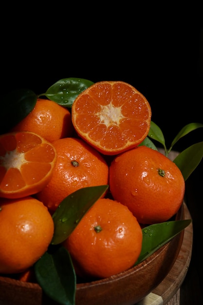 Cerca de mandarinas con hojas en un cuenco de madera