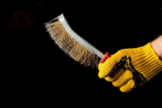 Cerca de la mano del artesano en un guante sostiene un cepillo para eliminar el óxido