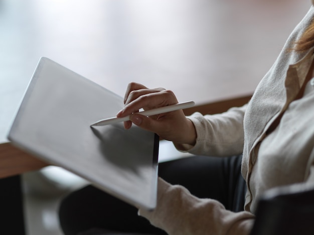 Cerca de la mano de la empresaria trabajando en tableta digital con lápiz óptico y fondo borroso