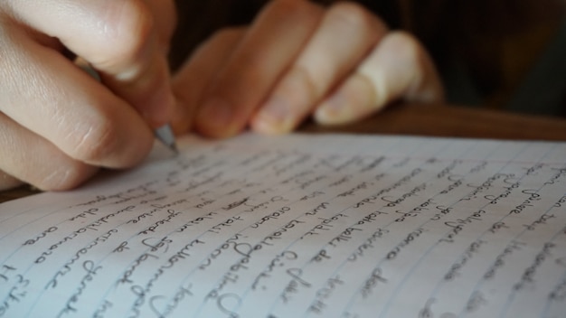 Cerca de la mano escribiendo en el cuaderno en el café