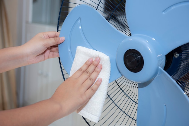 Cerca de la mano femenina que limpia la aspa del ventilador eléctrico sucio con un paño blanco