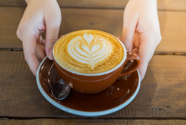 Cerca de la mano femenina que sirve café con arte latte en la mañana