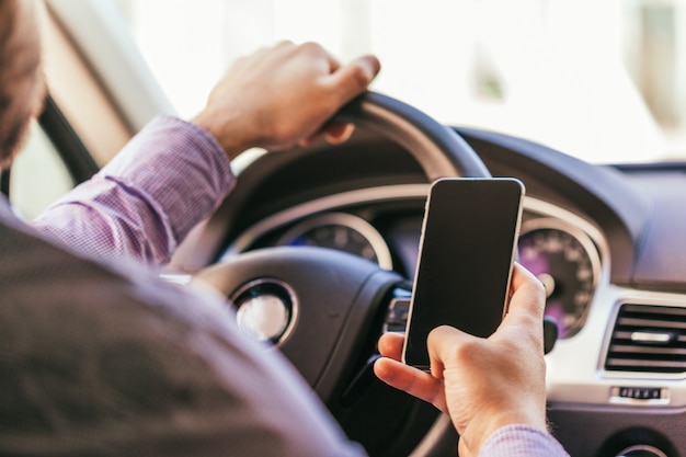 Cerca de la mano del hombre joven con smartphone conduciendo coche