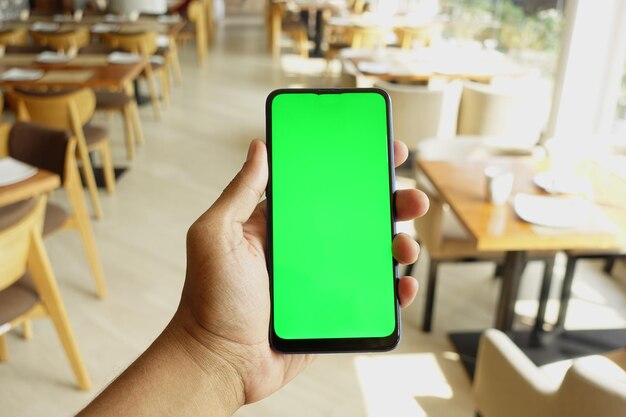 Cerca de la mano de un joven usando un teléfono inteligente con pantalla verde