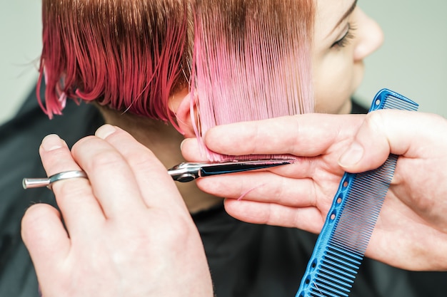 Foto cerca de una mano masculina es cortar el cabello rosado con unas tijeras.