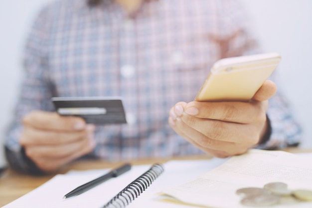 Foto cerca de la mano masculina que sostiene la tarjeta de crédito y el uso de banca por internet de computadora portátil. gastar dinero, comercio electrónico, compras en línea, trabajar desde el concepto de hogar.