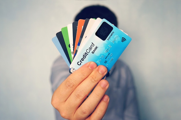 Cerca de la mano masculina sosteniendo la pila de tarjetas de crédito de muchos colores en desenfoque de fondo azul claro. Hombre mostrando tarjetas de pago de nueva generación. Tecnología de escaneo de huellas dactilares en banca. Muchos.