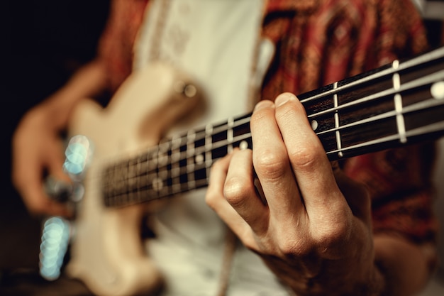 Cerca de la mano masculina tocando la guitarra eléctrica en la oscuridad