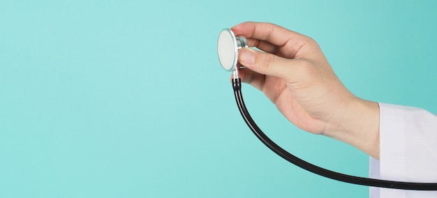 Foto cerca de la mano del médico sosteniendo un estetoscopio y use una bata de manga larga sobre fondo verde menta o azul tiffany